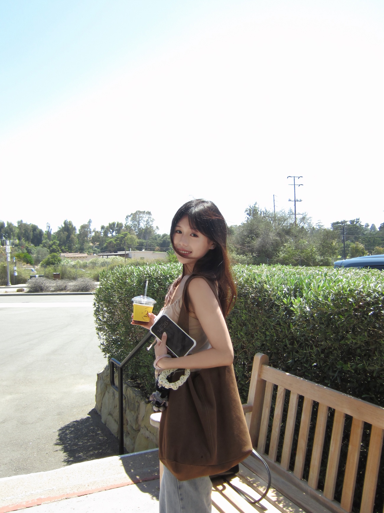 Picture of Yan holding a coffee by a bench with a park in the background.