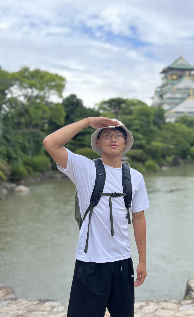 Picture of Dylan saluting to the camera, in front of a river wearing a bucket hat.