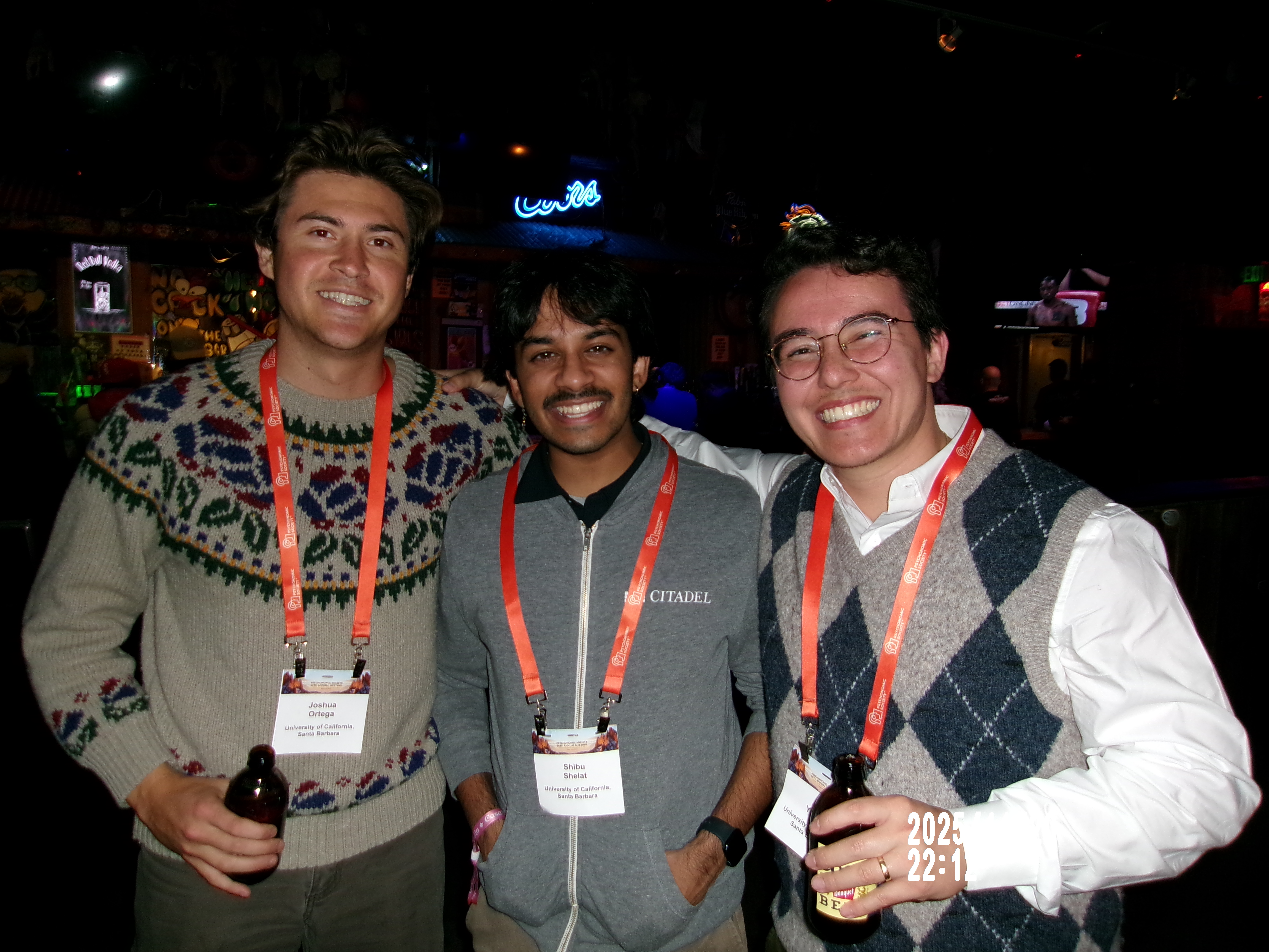 Three lab members smiling and holding drinks with psychonomics conference tags around their necks.